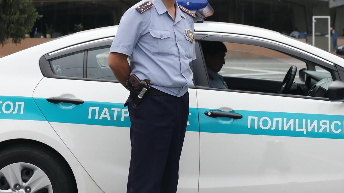 Полицейский в форме стоит возле служебного автомобиля