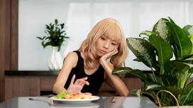 Хрупкая девушка безразлично смотрит на тарелку с едой