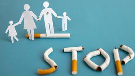 Прожженные бумажные фигурки семьи стоят рядом с надписью "STOP" из сигарет