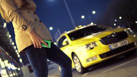 Девушка с телефоном в руках стоит на фоне машины такси