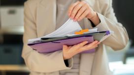 Девушка держит в руках папки с документами