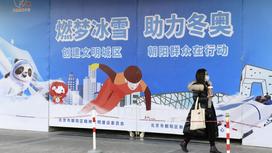 Женщина идет рядом с плакатом Олимпиады в Пекине