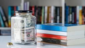 Стеклянная банка с долларами стоит возле стопки книг