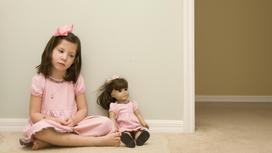 Девочка сидит у стены вместе с куклой