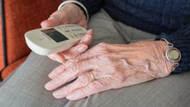 Пожилой мужчина держит в руке кнопочный телефон
