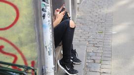 Девушка сидит за стеной с телефоном в руках