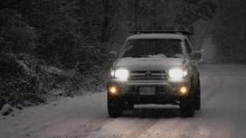 Автомобиль Toyota стоит на дороге зимой с включенными фарами