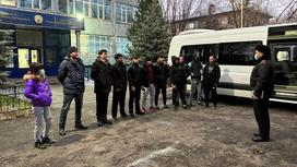 Мигранты стоят перед полицейским в Алматы