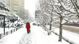 Женщина в красной одежде идет по заснеженной улице