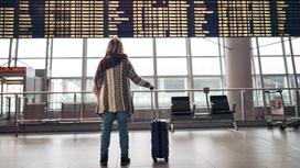 Женщина стоит в аэропорту с чемоданом