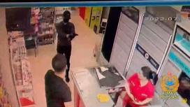 Мужчина в маске и кепке стоит с пистолетом в магазине