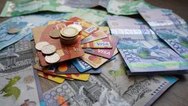 На столе лежат купюры тенге и банковские карты с монетами