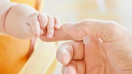Младенец держит взрослого за палец
