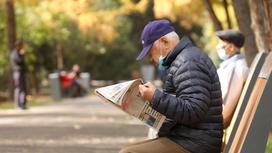 Пожилой мужчина сидит на скамейке и читает газету