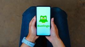 Девушка держит в руках смартфон с открытым приложением Duolingo