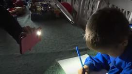 Ребенок делает уроки под свет фонарика на смартфоне