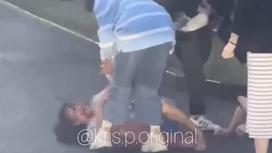 Люди пытаются поднять с земли девушку после драки в Алматы