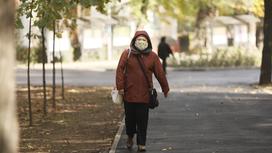 Женщина в куртке и маске идет по улице