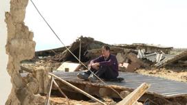 Мужчина сидит на руинах дома