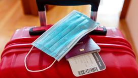 Паспорт, билет на самолет и медмаска лежат на красном чемодане
