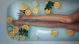 Женские ноги в ванной с кусочками цитрусовых