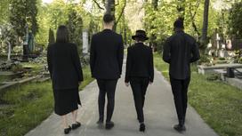Люди в черной одежде идут по кладбищу