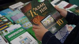 Человек держит учебник по казахскому языку за 10 класс