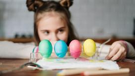 Девочка смотрит на окрашенные в разные цвета яйца, стоящие на столе