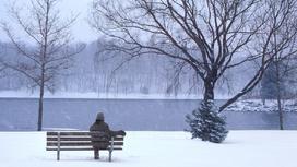 Человек сидит один на лавочке зимой