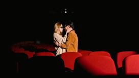 Влюбленная пара обнимается, стоя между рядами кресел в кинотеатре