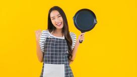Улыбающаяся девушка в фартуке со сковородой в руке