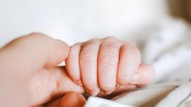 Рука младенца держит палец женщины