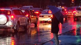 Человек под зонтом стоит у обочины дороги