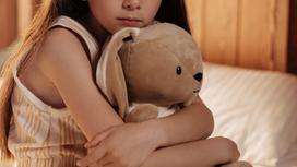 Девочка сидит на кровати и держит игрушку в руках