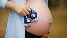 Беременная женщина держит в руках пинетки