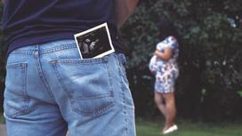 Мужчина стоит напротив беременной женщины со снимком УЗИ в кармане