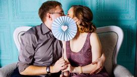 Мужчина и женщина целуются, прикрывшись бумажным веером