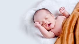 Новорожденный лежит на белом одеяле