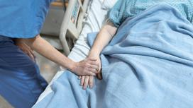 Медик держит женщину за руку в больничной палате