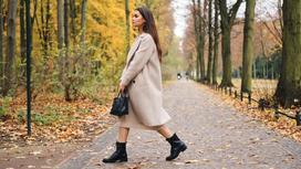 Девушка в светлом пальто и ботинках гуляет по осеннему парку