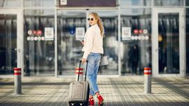 Красивая девушка с чемоданом стоит у входа в аэропорт