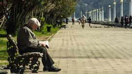 Пожилой мужчина читает газету на скамье в парке
