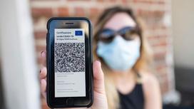 Девушка в маске держит телефон с паспортом вакцинации