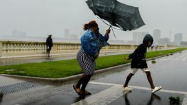 Женщина с зонтом и мальчик идут по дороге во время сильного ветра