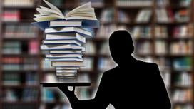 Книги сложены одна на другую на подносе. Мужчина держит поднос на одной руке возле стеллажей с книгами держит стопку книг на руке