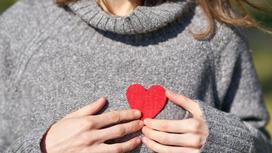 Девушка в сером свитере держит красное сердце