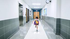 Девчока с рюкзаком бежит по коридору школы