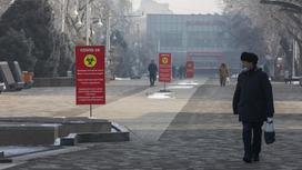 Люди идут по улице с баннерами с информацией по коронавирусу в Алматы
