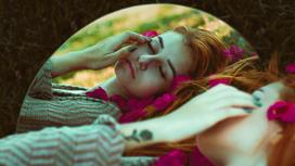 Девушка лежит с закрытыми глазами в поле, повернувшись к своему отражению в зеркале