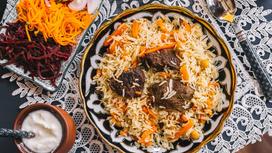 Узбекский плов с бараниной на сервировочном блюде, поданный с овощными закусками
